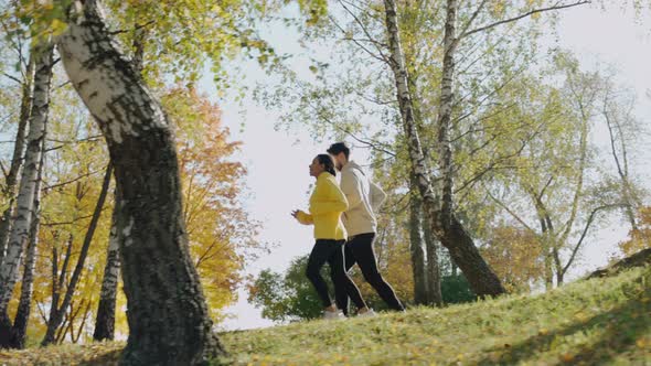 Young Woman and Man Running on the Stairs at the Park in Sunny Autumn Morning