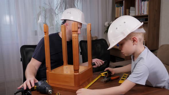 A Little Boy with His Father in White Helmets Fixing a Wooden Chair Together