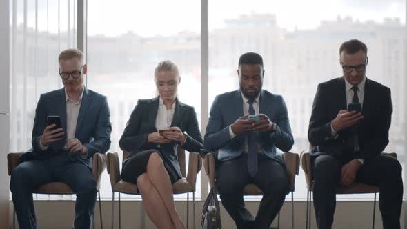 Diverse Applicants in Formal Wear Waiting for Job Interview Using Mobile Devices