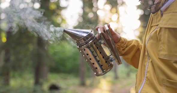 A Beekeeper Dressed in a Protective Suit with a Mosquito Net Over His Head Sprays White Smoke Over