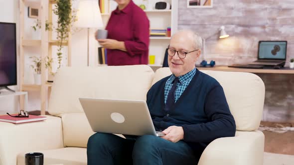 Elderly Age Couple with Glasses Sitting on Sofa During a Video Call on Laptop.