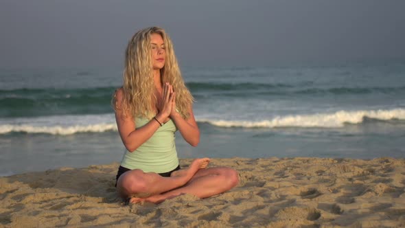 A young woman doing yoga on the beach while sitting.