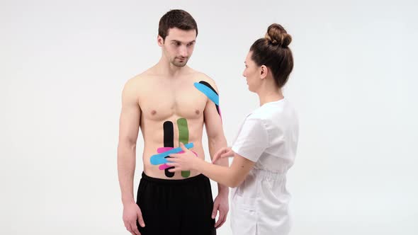 Female therapist applying kinesiology tape on a man's abdomen on the white background