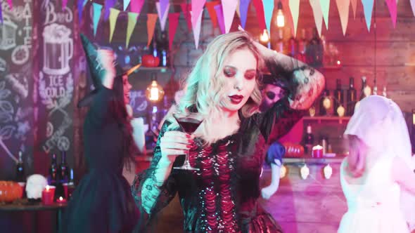 Young Pretty Woman with a Glass of Blood in Her Hand Dancing at a Halloween Party