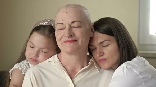 An Adult Daughter and Little Granddaughter Hug a Sad Elderly Woman Who Has Gone Bald After