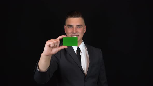 A Young Businessman in a Suit Holds a Bank Card in Hand. Isolated Black Background. Chromakey Green