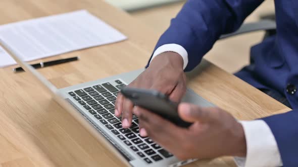 Close Up of African Businessman Using Smartphone and Laptop