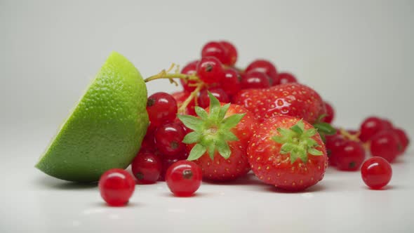 A Slice Of Lime, Three Sweet Strawberries And A Bunch Of Red Currants On Top Of The Table - Close Up