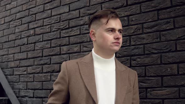 Portrait of a Handsome Fashionable Man in Brown Coat Against a Brick Wall Background