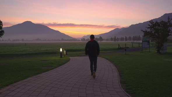 Man Walking Along Footpath Towards Misty Landscape At Dawn