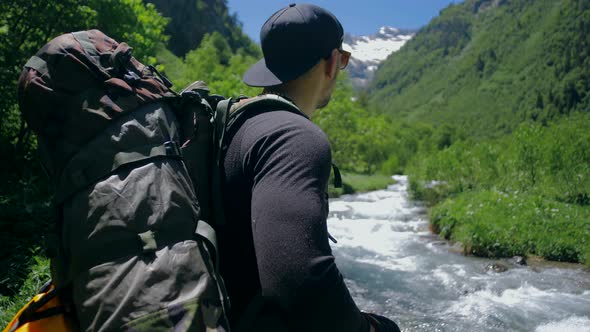 Traveler with a large backpack is standing by the mountain river