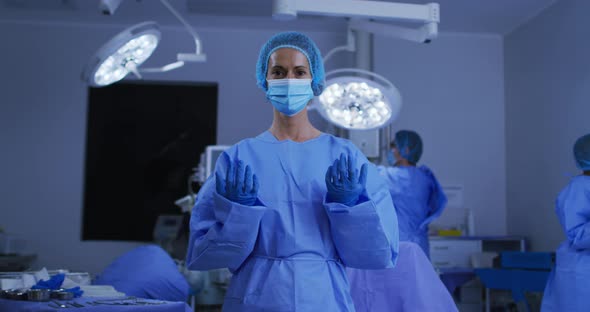 Portrait of caucasian female surgeon wearing face mask and protective clothing in operating theatre