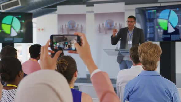 Woman in audience at a business conference filming with smartphone