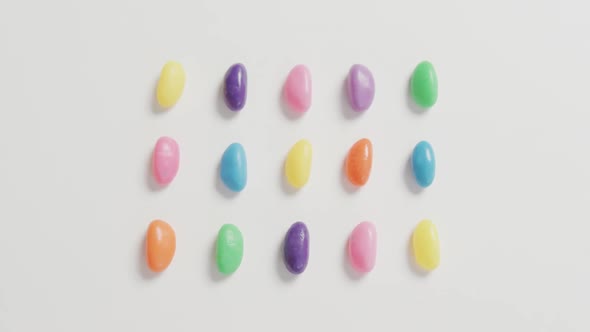 Video of overhead view of rows of multi coloured sweets over white background