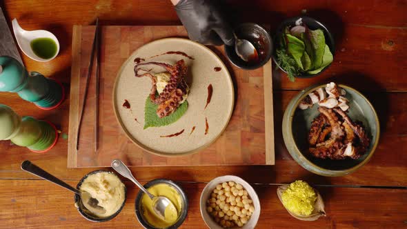 Top down view of a sophisticated professional fine dinning chef plating the smoked octopus and drizz