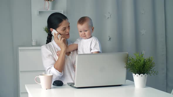 Young Mother Holding Baby While Working in Home Office