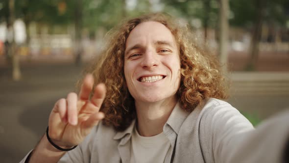 Smiling curly-haired man showing different gestures at the camera