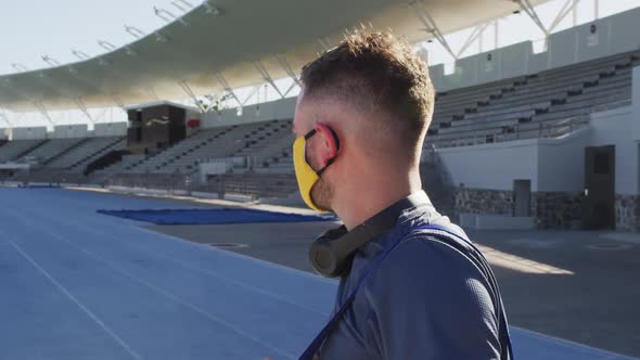 Caucasian male athlete wearing face mask and headphones on sunny day