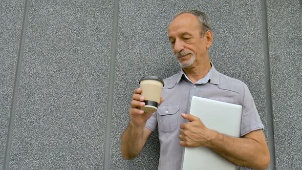 Male Portrait of Older Coworker with Silver Laptop and Cup of Coffee Waiting for a Meeting Near Dark