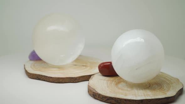 Two Round White Crystals Sitting On A Piece Of Wood With Small Gem Stones Beside - Close Up Shot