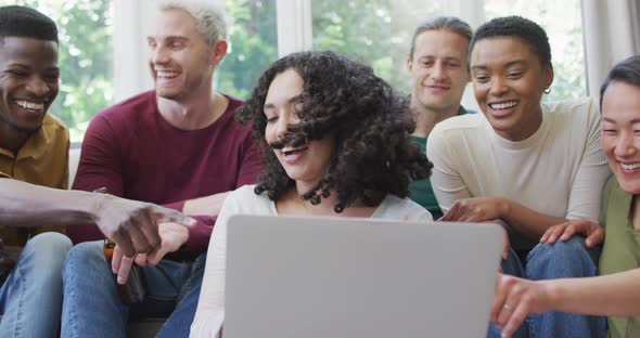 Diverse group of happy male and female friends looking at laptop and laughing in living room