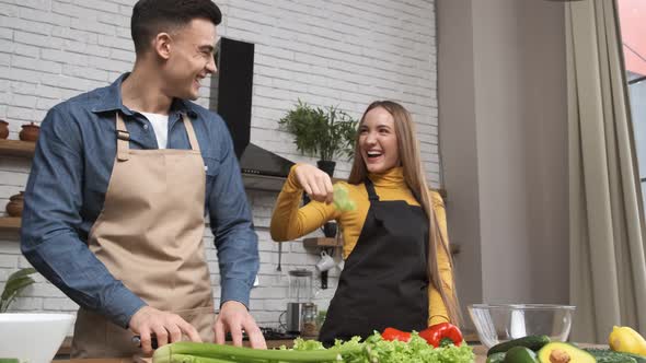 Cooking Salad at Home Young Couple Laughing and Fooling Around with Vegetables in Modern Kitchen