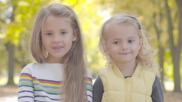 Two Little Caucasian Girls Standing in the Autumn Park and Looking at the Camera