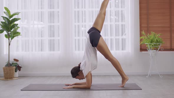 Yoga  Handstand Posture, Vrischikasana on mat, Asian woman in sportswear working out inside.