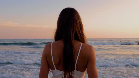 Beautiful woman in a white dress at the beach at sunset