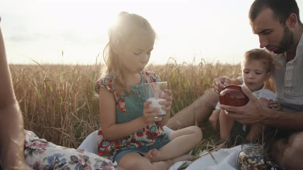 A Friendly Family with a Daughter and a Small Son is Having Lunch at a Picnic in a Wheat Field on a