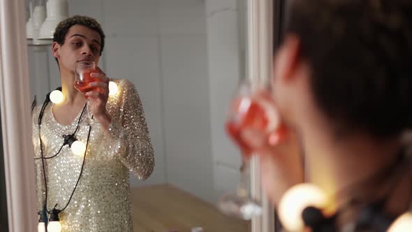 A Man in a Dress Posing in Front the Mirror with Garland on Neck and Glass of Wine