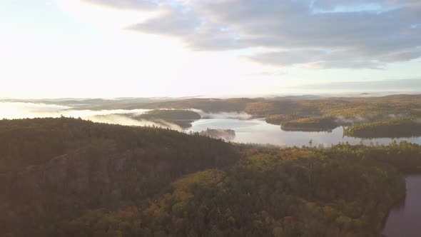 Aerial Sunrise Wide Shot Flying Over Fall Forest Colors Toward Misty Lakes With Fog Covered Islands