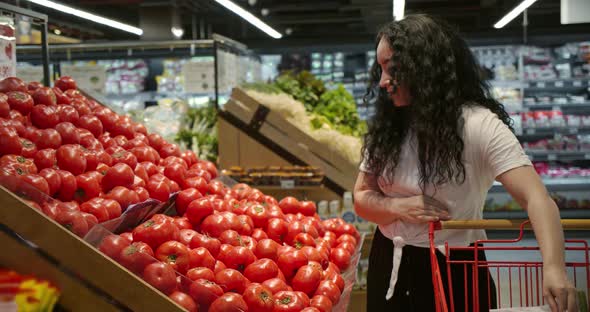 Young Woman in the Grocery Section of a Supermarket Picks Up a Bag and Puts Tomatoes in a Basket to