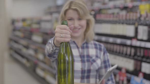 Focus Changes From Pretty Face of Smiling Caucasian Blond Woman To the Bottle of White Wine