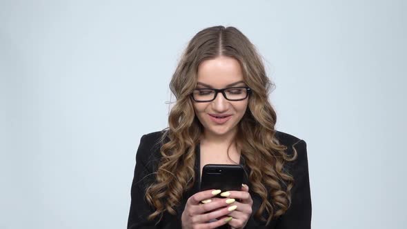 Young Smiling Woman Texting on Her Phone on Gray Background in Studio, Slow Motion