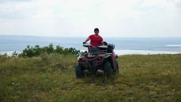 Man in a Black Cap and Red T-shirt on a Colored ATV Rides