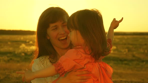 Happy Mother Walks with Her Daughter in Her Arms in the Rays of the Sunset. Mom Is Talking with