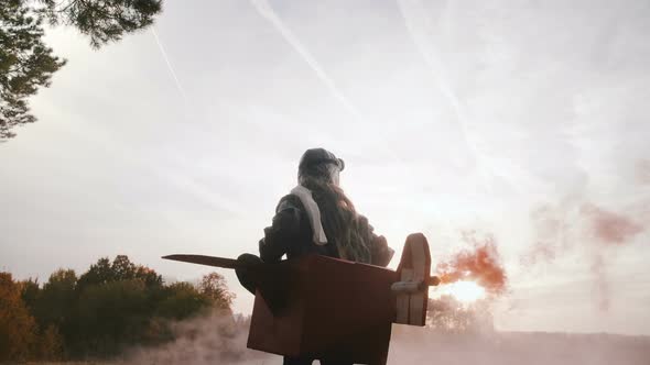 Low Angle Camera Follows Little Girl Running in Fun Cardboard Plane Pilot Costume with Color Smoke