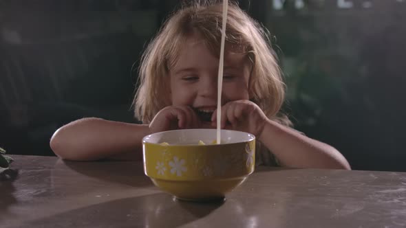 girl sits at wooden table and watches as milk is poured into Cup of cornflakes.