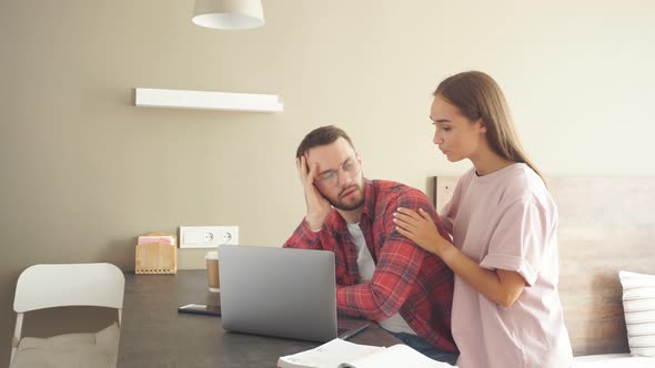 Upset Male Sits at Black Wooden Table Stares at Computer with Dissatisfied Feeling