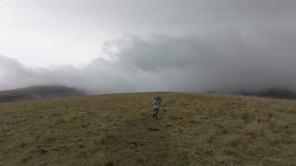 A Slender Young Woman in Travel Clothes Walks and Runs on a High Plateau in Foggy Weather Against