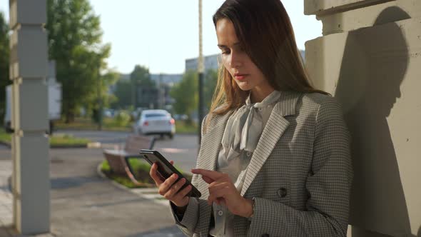 Young Woman in a Business Suit with a Phone Stands on the Street