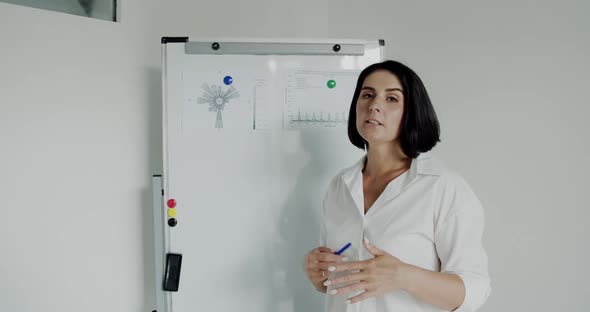 Female Speaker Conducts Lecture in Front of Camera at Whiteboard in Office