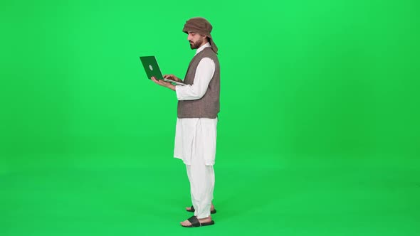 Freelancer Man of Arab Appearance in Traditional Clothes Uses a Laptop to Surf the Internet While