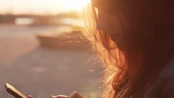 Young attractive business woman sitting outdoor on the bench and using smartphone.