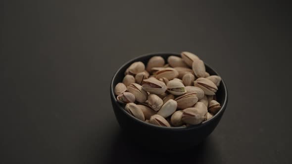 Handheld Slow Motion Salted Large Pistachios in Black Bowl on Black Paper Background