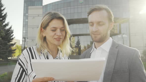 Two Business Colleagues Examining Documents Outdoors in Front of Office Building