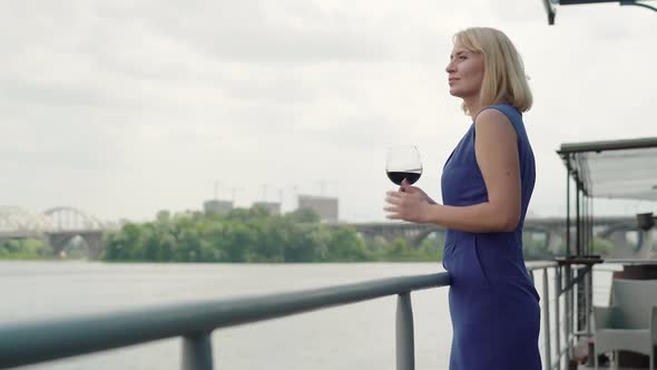 Side View of Confident Thoughtful Lady Standing on River Bank with Wineglass and Looking Away