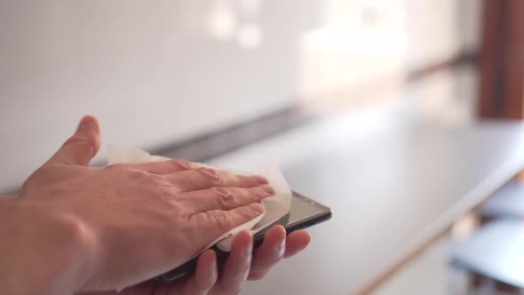 young man disinfects a black smartphone with a white napkin in a bright room.