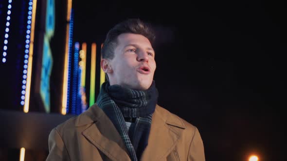 Happy Smiling Man in Brown Coat Walks on Winter Night Along Street Glowing City